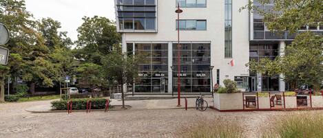 A modern building with a glass facade, a paved courtyard, and a red bollard.
