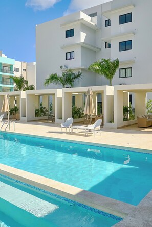 A swimming pool with lounge chairs and umbrellas, surrounded by a modern building with balconies. - Cozy studio in gated community near Downtown Punta Cana (Punta Cana)