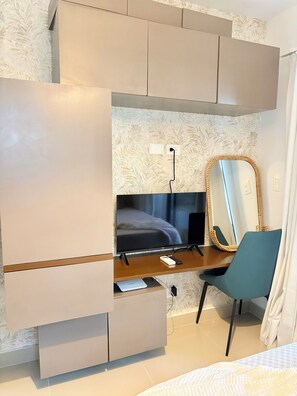 A bedroom with a bed, a desk with a computer, a chair, a mirror, and built-in storage. - Cozy studio in gated community near Downtown Punta Cana (Punta Cana)