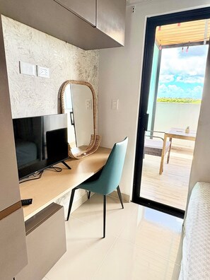Ein modernes Zimmer mit Flachbildfernseher, einem blauen Sessel, einem dekorativen Spiegel und Blick ins Freie durch eine Schiebetür.