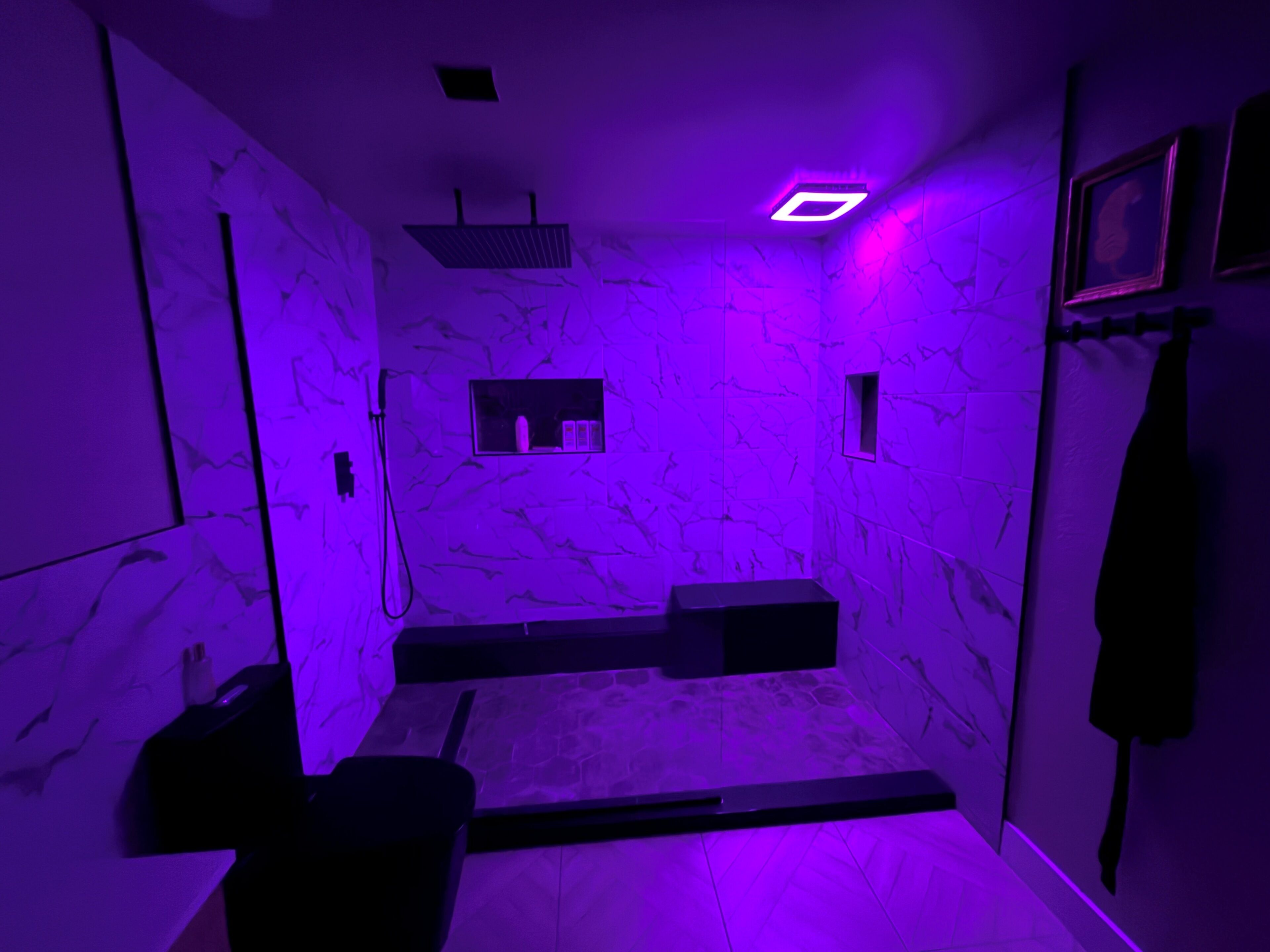 A room with a marble wall, a built-in shelf, and a shower area.