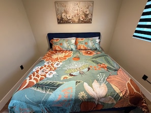 Ein Bett mit einem blumigem Überwurf, einem Kopfteil und einem an der Wand hängenden Kunstwerk.