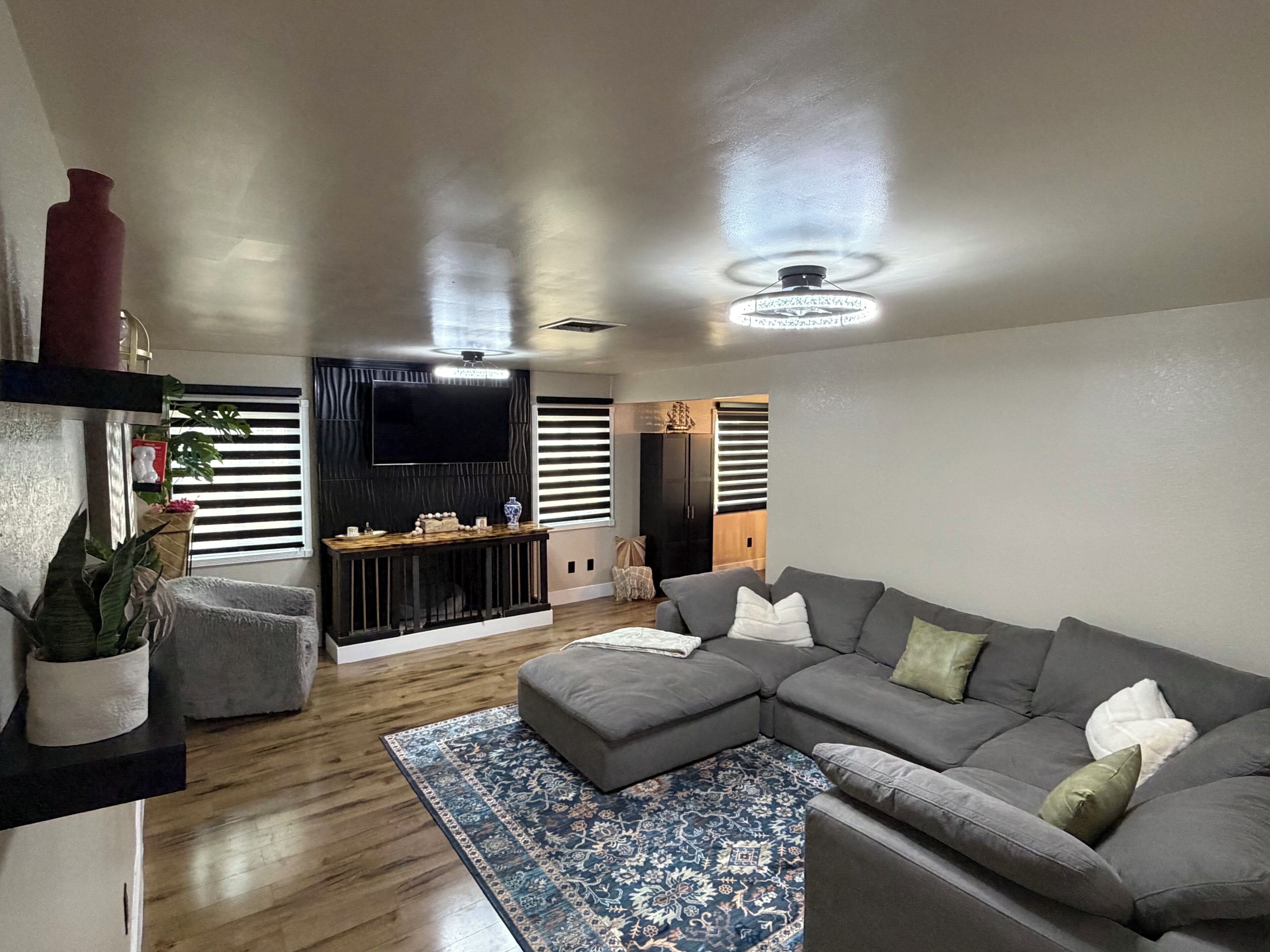 A modern living room with a sectional sofa, a flat-screen TV mounted on the wall, a wooden coffee table, and a patterned rug.