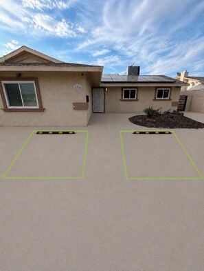 Un immeuble résidentiel à la façade beige, doté d’un portail de garage et d’un petit jardin planté.