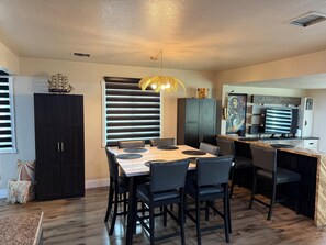 Une cuisine moderne avec un coin repas, comprenant un grand îlot central, des meubles de couleur noire et un luminaire original.