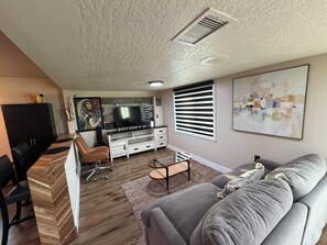 Ein modernes Wohnzimmer mit Sofa, Fernseher und einem Essbereich mit Stühlen und einem Schrank.