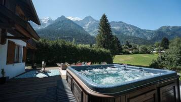 A hot tub with a mountain view, a wooden deck, and a pool.