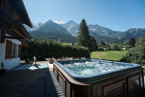 Un bain à remous avec vue sur les montagnes, une terrasse en bois et une piscine.