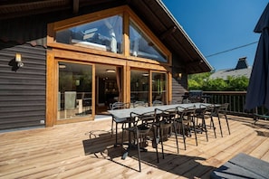 A wooden deck with a table and chairs, a glass door entrance, and a barbecue grill. - Chalet with a view of Mont Blanc | Sleeps 10 | Sauna | Hot tub (Les Houches)