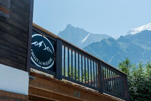 Holzgeländer eines Balkons mit einem Schild, auf dem 'CHALET LA MURAINE' steht, vor einer Kulisse schneebedeckter Berge.
