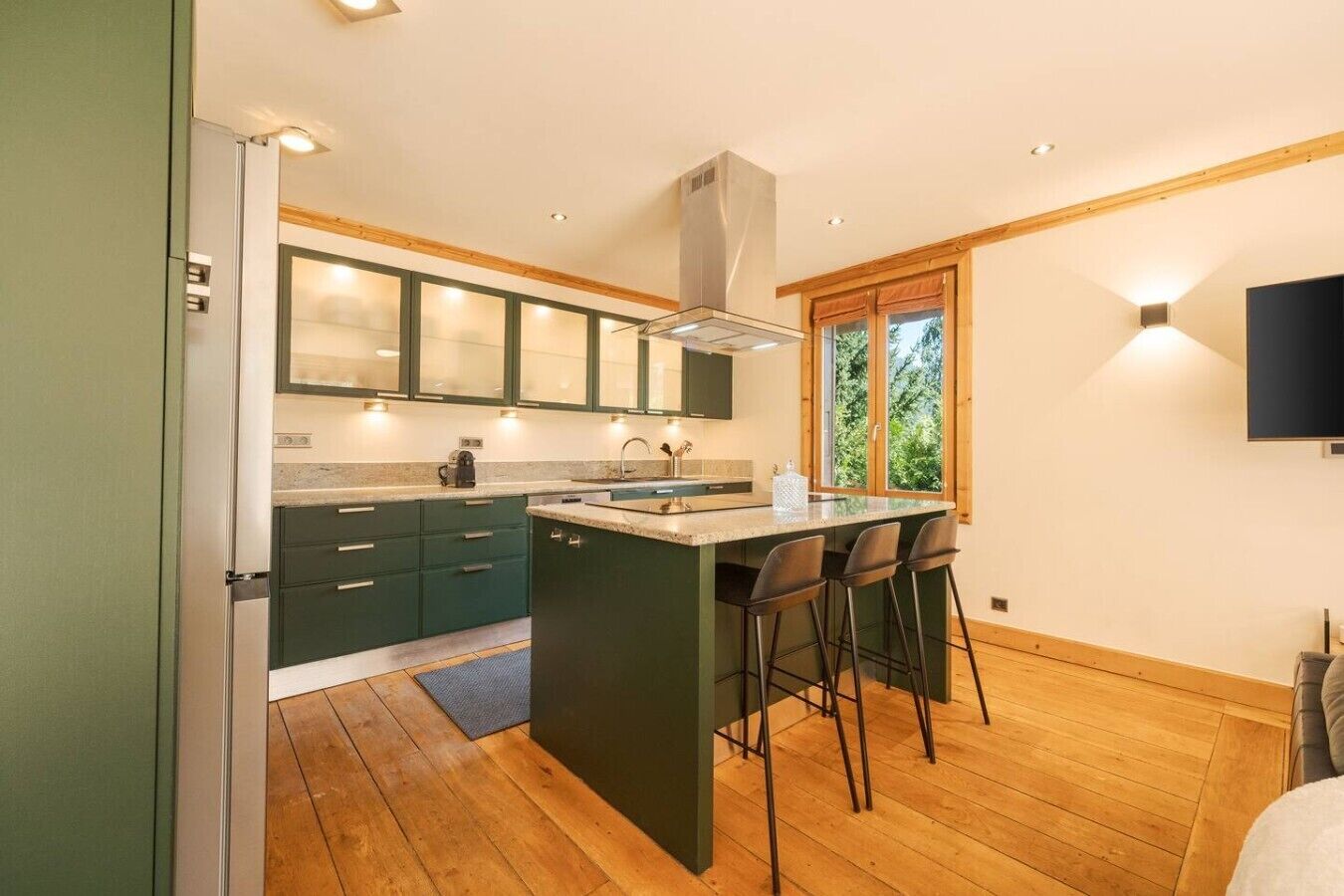 Una cocina moderna con una isla central, taburetes de bar y una ventana que ofrece vistas a zonas verdes.
