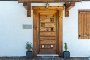 Une porte en bois avec une poignée en métal, une petite enseigne au-dessus, et deux plantes en pot de chaque côté.