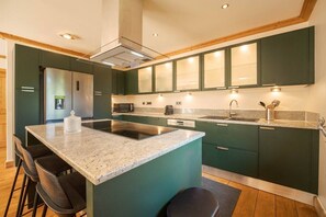 A modern kitchen with a central island, dark green cabinets, stainless steel appliances, and a granite countertop. - Chalet with a View of Mont Blanc | Sleeps 10 | Sauna | Hot Tub (Les Houches)