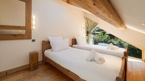 Ein Schlafzimmer mit zwei Betten, Holz-Kopfteilen, Holzboden und einem Fenster mit Blick auf Grünflächen.