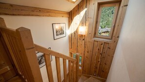Eine Holztreppe mit Handlauf, ein kleines Fenster mit Blick auf Grünflächen und gerahmte Bilder an der Wand.