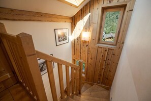 A wooden staircase with a handrail, a small window with a view of greenery, and framed pictures on the wall. - Chalet with a View of Mont Blanc | Sleeps 10 | Sauna | Hot Tub (Les Houches)