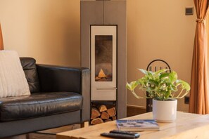 A living room with a black leather sofa, a white throw pillow, a wooden coffee table with a remote control and a book, a potted plant, and a fireplace with a mantel. - Chalet with a View of Mont Blanc | Sleeps 10 | Sauna | Hot Tub (Les Houches)