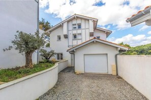 Ein zweistöckiges Haus mit Garage, einem Schotterweg und einem Baum im Vordergrund.