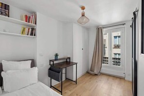 A bedroom with a bed, a desk, a bookshelf, and a window with a view. - Central and Bright 1BR- Near Parc Monceau (Paris)