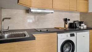 Een kleine keuken met een ingebouwde wasmachine, een spoelbak en houten kastjes.