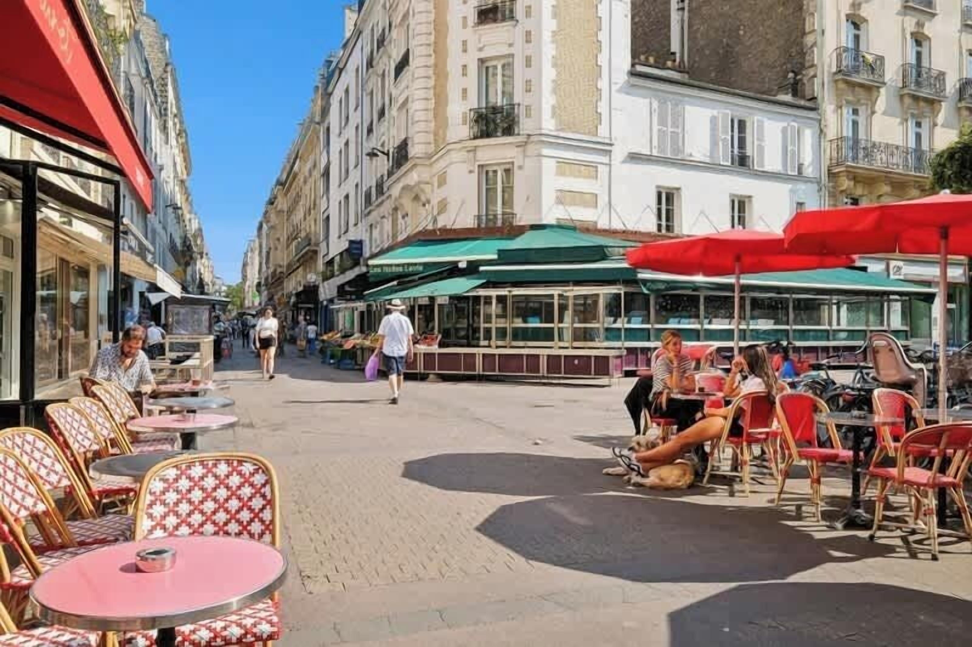 Un café en plein air, avec des tables et des chaises, entouré d’immeubles.
