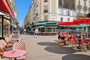 An outdoor café with tables and chairs, surrounded by buildings. - Central and Bright 1BR- Near Parc Monceau (Paris)
