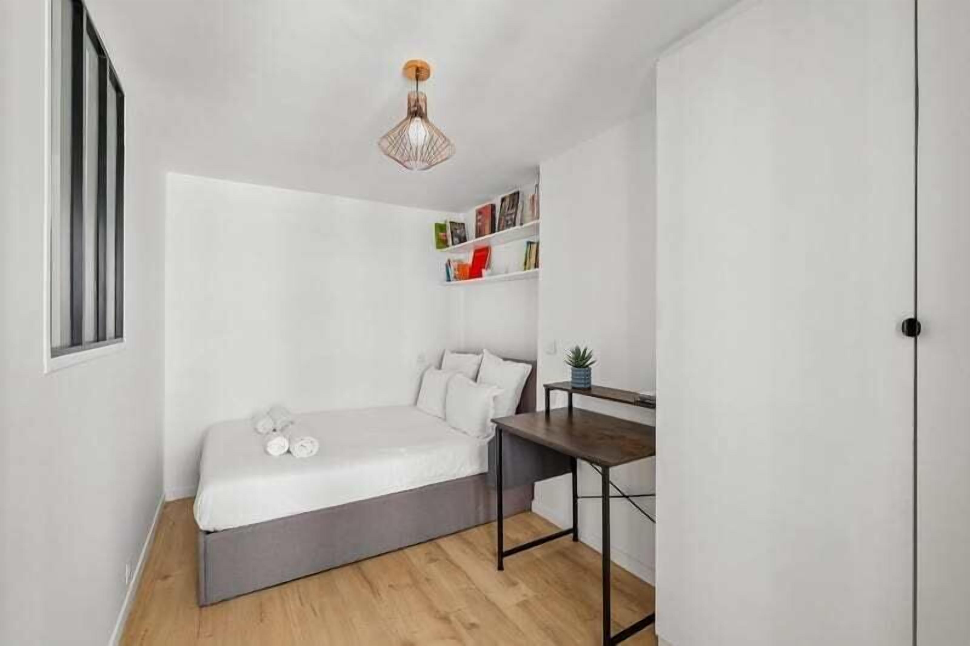 A small, compact room with a bed, a desk, and a bookshelf.
