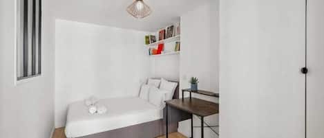A small, compact room with a bed, a desk, and a bookshelf.
