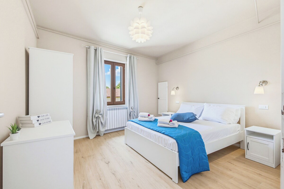 Un dormitorio moderno con cama, mesitas de noche, un escritorio y un ventanal con cortinas.