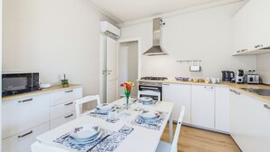 Moderni keittiö, jossa on valkoiset kaapit, mikroaaltouuni, liesi ja kahvinkeitin.
