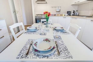 Een eettafel gedekt met borden, bestek en een bloemenvaas, met een keuken op de achtergrond.