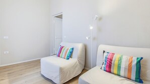 Minimalistinen huone, jossa on kaksi valkoista sohvaa, ja jokaisessa on värikäs raidallinen koristetyyny. Lisäksi huoneessa on valkoinen kattovalaisin ja puulattia.