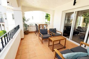 A balcony with a tiled floor, a wooden table, two chairs, a sofa, and a potted plant. - Well Furnished West-Facing 2 Bed 1 Bath Apartment (Sucina)