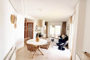 A bright living room with a round dining table, a sofa, and a view of the outdoors. - Well Furnished West-Facing 2 Bed 1 Bath Apartment (Sucina)