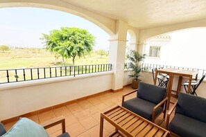 Ein Balkon mit Blick auf einen Baum und einen Golfplatz, ausgestattet mit einem Tisch und Stühlen.