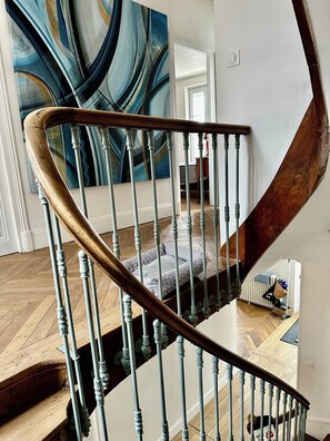 A spiral staircase with a wooden handrail and metal balusters, leading to a room with a large abstract painting. - Manor house + swimming pool (Meyssac)