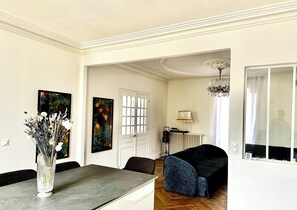 A dining area with a table and chairs, a vase with flowers, and two paintings on the wall.