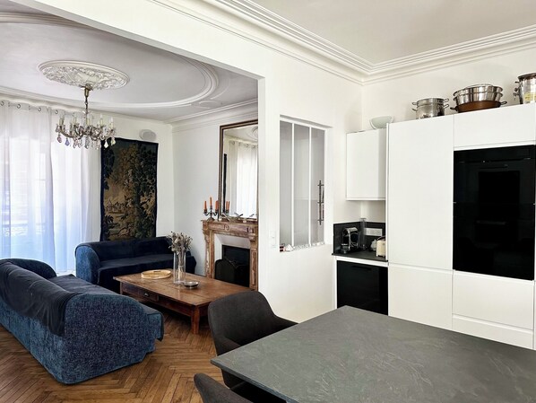 A modern living room with a sofa, a dining table, and a kitchen area with cabinets and appliances.