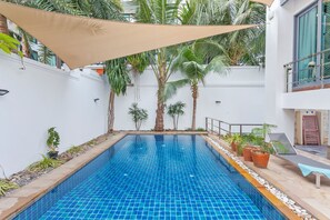 A swimming pool with a tiled floor, surrounded by plants and a white wall. - Angels -  Luxurious 4-bedroom villa Pattaya sleeps 8 people (Muang Pattaya)