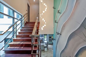 Un escalier avec une rampe en métal, un mur orné d’un motif ondulé original et une série de luminaires suspendus.