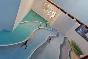 Un intérieur moderne avec un plafond au design original, évoquant une vague, un luminaire central et une plante en pot.