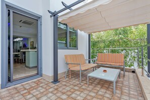 An outdoor patio with a tiled floor, a table, two striped chairs, a sofa, and a covered area with a view of greenery. - Angels -  Luxurious 4-bedroom villa Pattaya sleeps 8 people (Muang Pattaya)