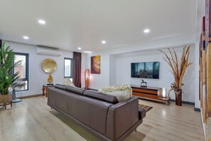 A modern living room with a leather sofa, a flat-screen TV, and a large window. - Angels -  Luxurious 4-bedroom villa Pattaya sleeps 8 people (Muang Pattaya)