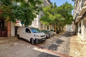 Eine schmale Straße gesäumt von parkenden Autos und Bäumen, mit Häusern an beiden Seiten.