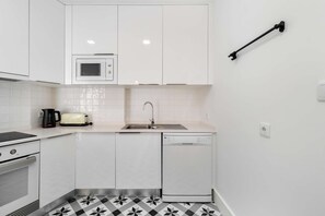Une cuisine de taille réduite avec des meubles blancs, un four à micro-ondes, un grille-pain, un évier et un lave-vaisselle.