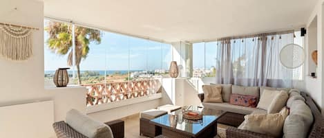 A modern living room with a glass coffee table, wicker furniture, and a view of the city.