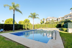 A swimming pool with a clear blue water surface, surrounded by a well-maintained lawn and palm trees. - RDR576 - Sea Views 2 Bed Apartment in Sea&Sun Hills (Estepona)