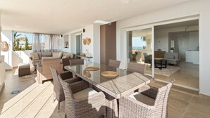 A spacious living area with a glass dining table surrounded by wicker chairs, a sofa, and a coffee table. - RDR576 - Sea Views 2 Bed Apartment in Sea&Sun Hills (Estepona)