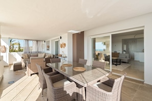 A spacious living area with a glass dining table surrounded by wicker chairs, a sofa, and a coffee table. - RDR576 - Sea Views 2 Bed Apartment in Sea&Sun Hills (Estepona)
