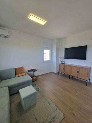 A living room with a sofa, ottoman, TV, and wooden cabinet. - Holiday apartment with garden and air conditioning (Turanj)